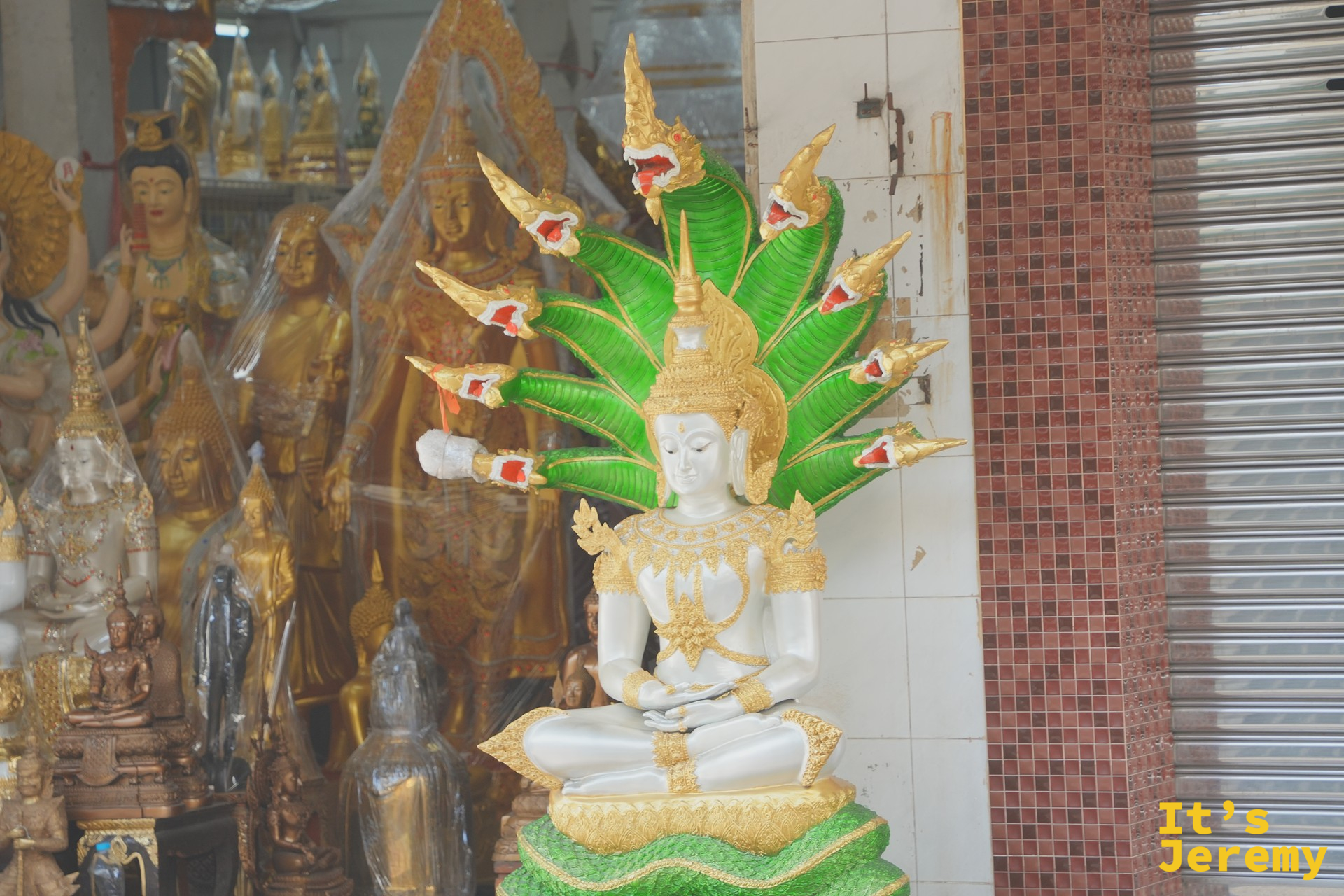 店門口立著一尊白色佛像、頭頂上是七條綠色那伽蛇神光環，這是泰國最具代表性的造像之一
