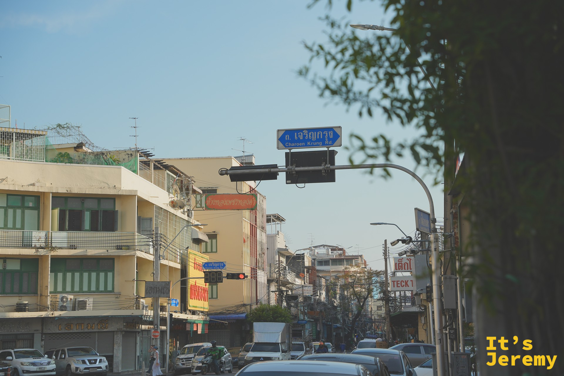 「ก. เจริญกรุง Charoen Krung Rd」的藍底路牌、傍晚的金光把樹葉切成幾條金邊