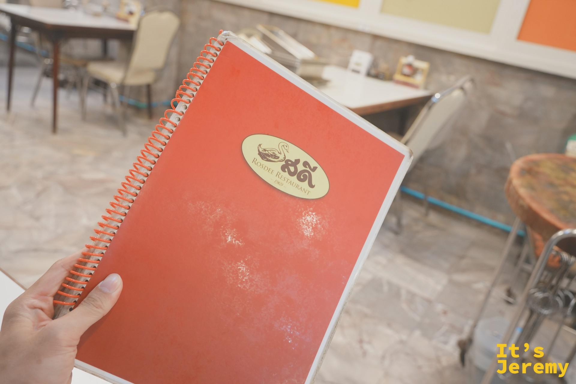 Rosdee Restaurant 橘紅色 spiral-bound 菜單與店內粉色座椅