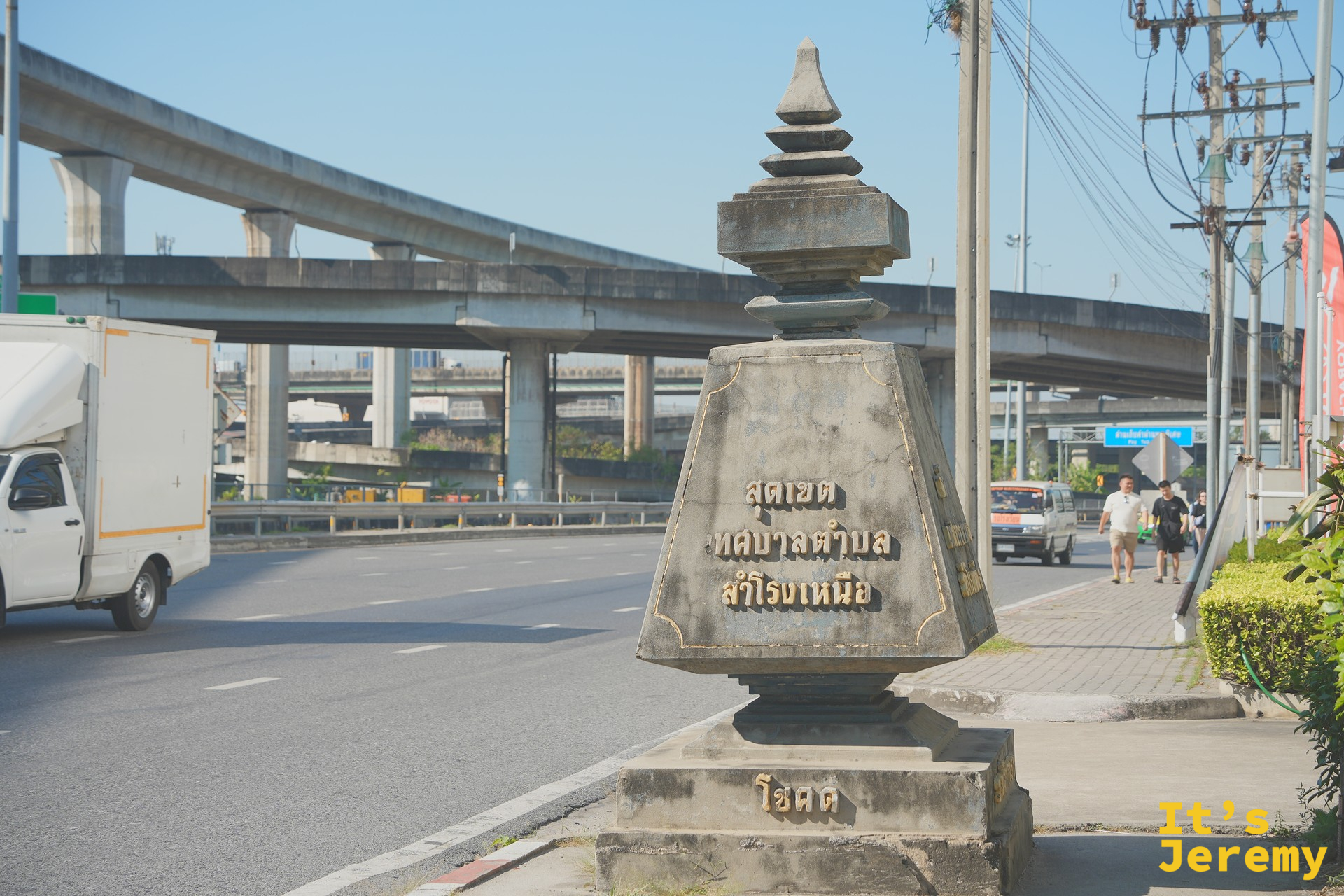 馬路邊的「Samrong Nuea 市鎮邊界」傳統石碑,背景是 BTS 高架軌道
