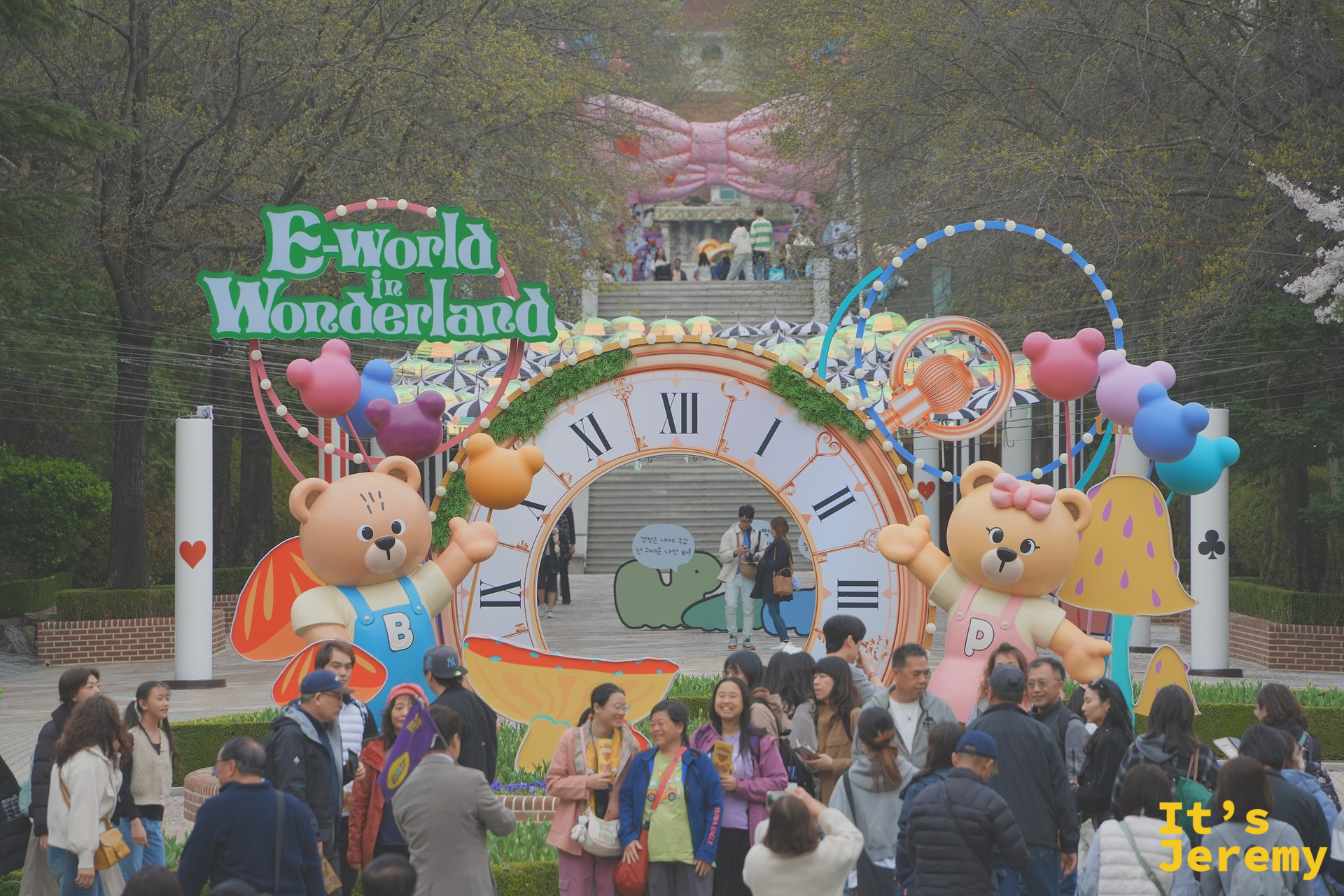 E-world in Wonderland 入口拱門:彩繪時鐘、左右兩隻 E-World 30 週年吉祥熊(左棕熊持「B」字、右粉熊持愛心球),彩色氣球綴在拱門上方,白天人潮聚集