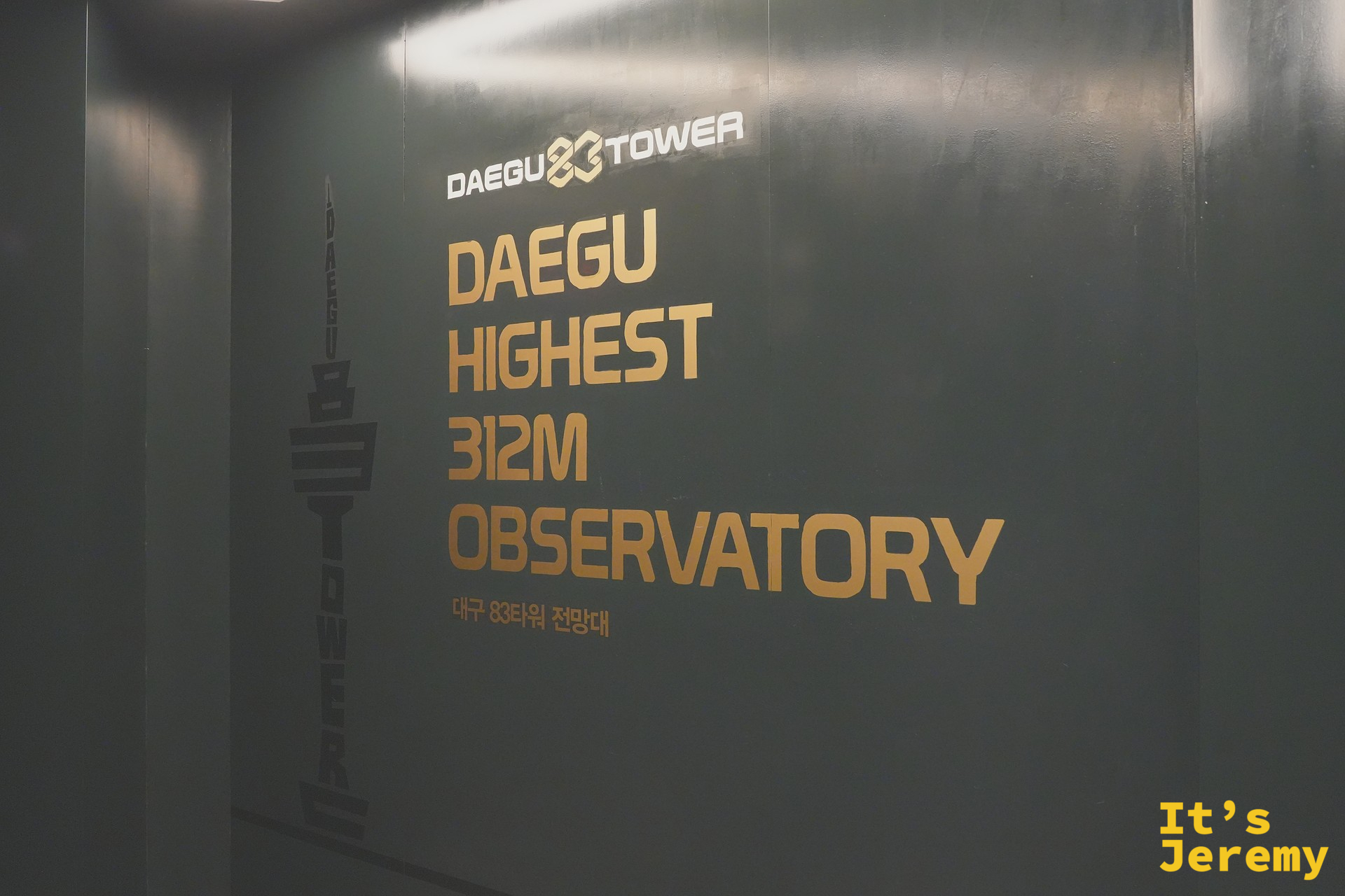83 塔觀景台入口的深綠色牆面,正中央印著金色英文「DAEGU HIGHEST 312M OBSERVATORY」與底下小字韓文「대구 83타워 전망대」,牆面左側有 Daegu Tower 的塔身剪影標誌