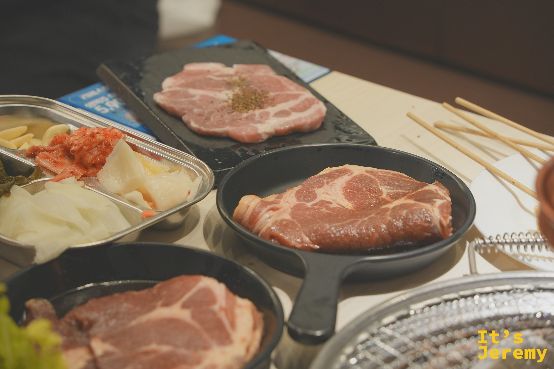 鑄鐵小盤盛著삼겹살與목살,旁邊是整套醃製小菜:大蒜、芝麻葉、泡菜、醃白蘿蔔