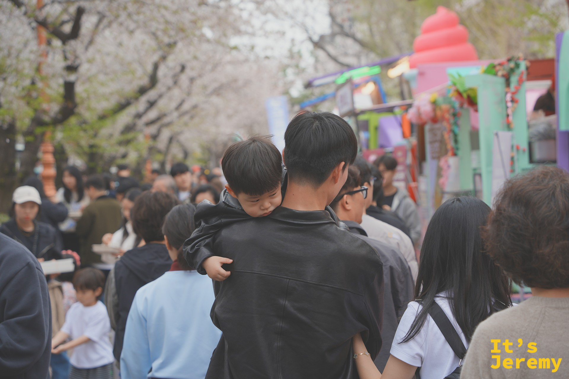 爸爸背著已經打瞌睡的小孩繼續在花道人群中穿行,右側是五顏六色的食物攤車——這個畫面大概是軍港祭最溫馨的紀實角度