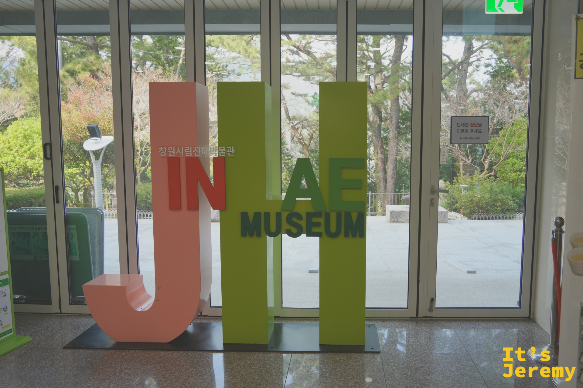 昌原市立鎮海博物館館內大廳,JINHAE MUSEUM 字樣裝置立於入口,落地窗外透著春日的綠意