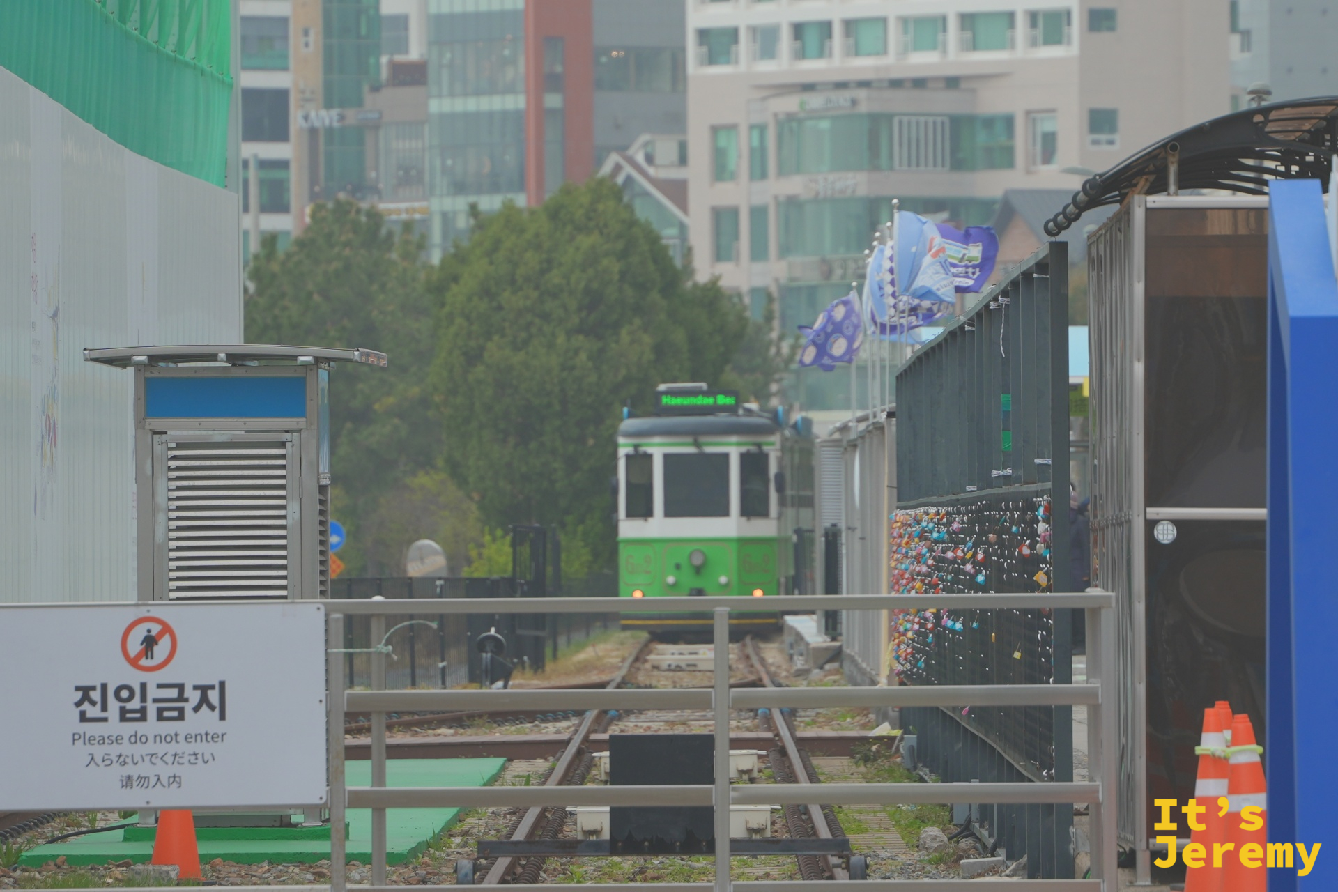 綠色海岸列車沿著雙軌鐵路緩緩駛入松亭站，右側可見掛滿愛情鎖的牆面