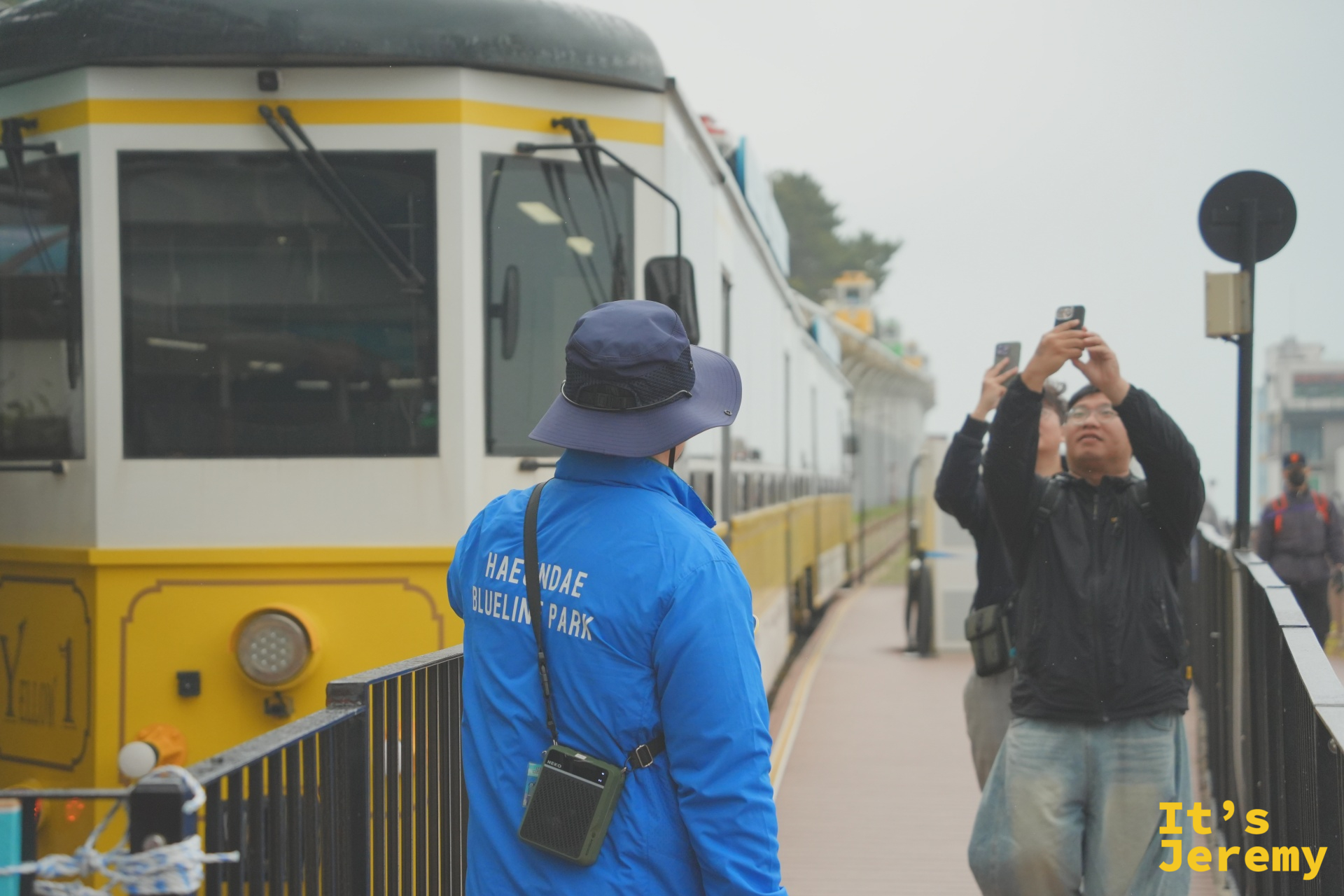 黃色海岸列車停在月台旁，工作人員引導乘客上車，旁邊還停著綠色車廂一同待命