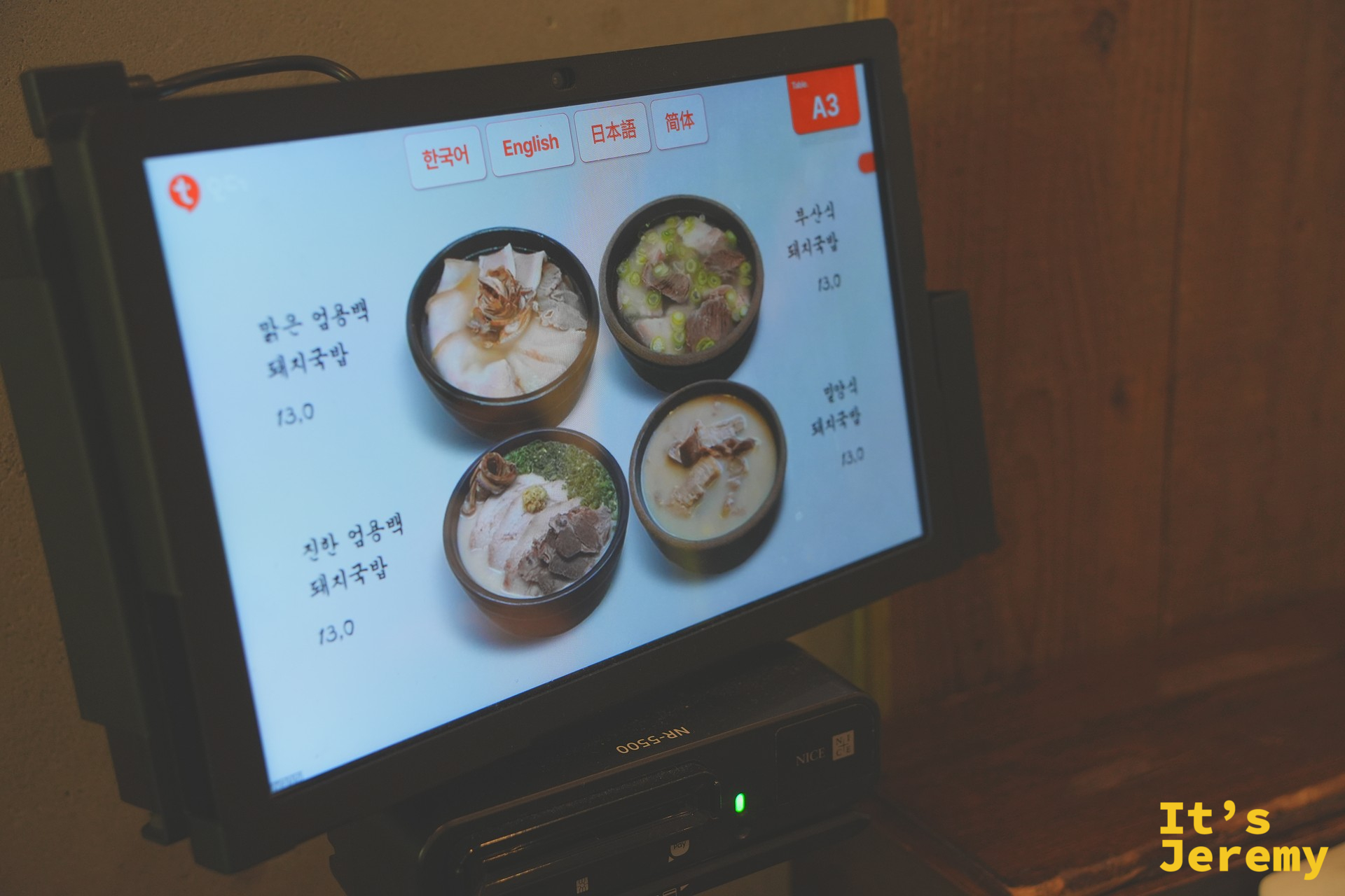 座位桌上的平板點餐機,顯示四款豬肉湯飯選項與照片,介面提供韓英日中四種語言