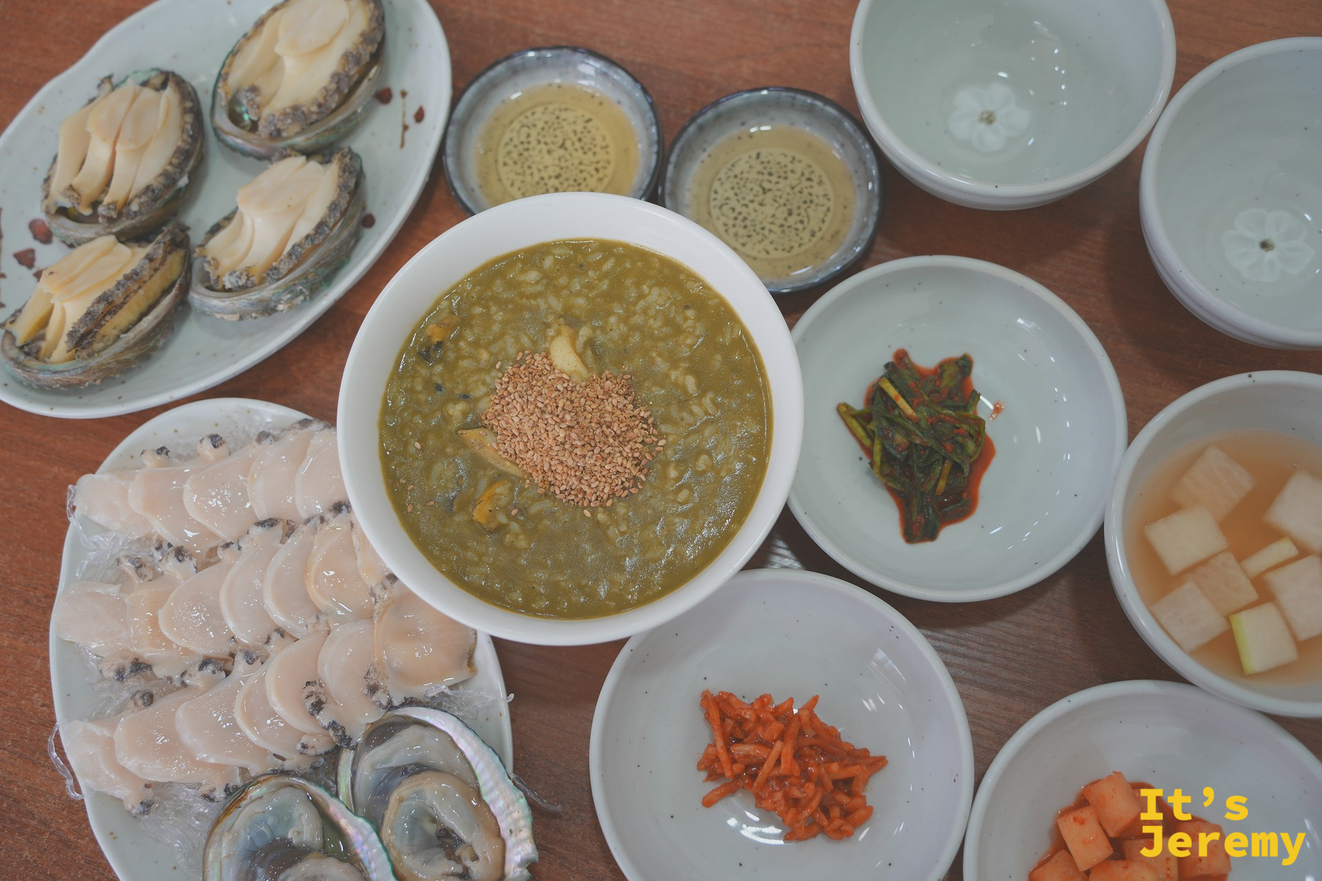全桌俯拍：左方찐전복蒸鮑魚、中央전복죽鮑魚粥、下方전복회刺身，小菜圍繞四周，主食配角各就各位