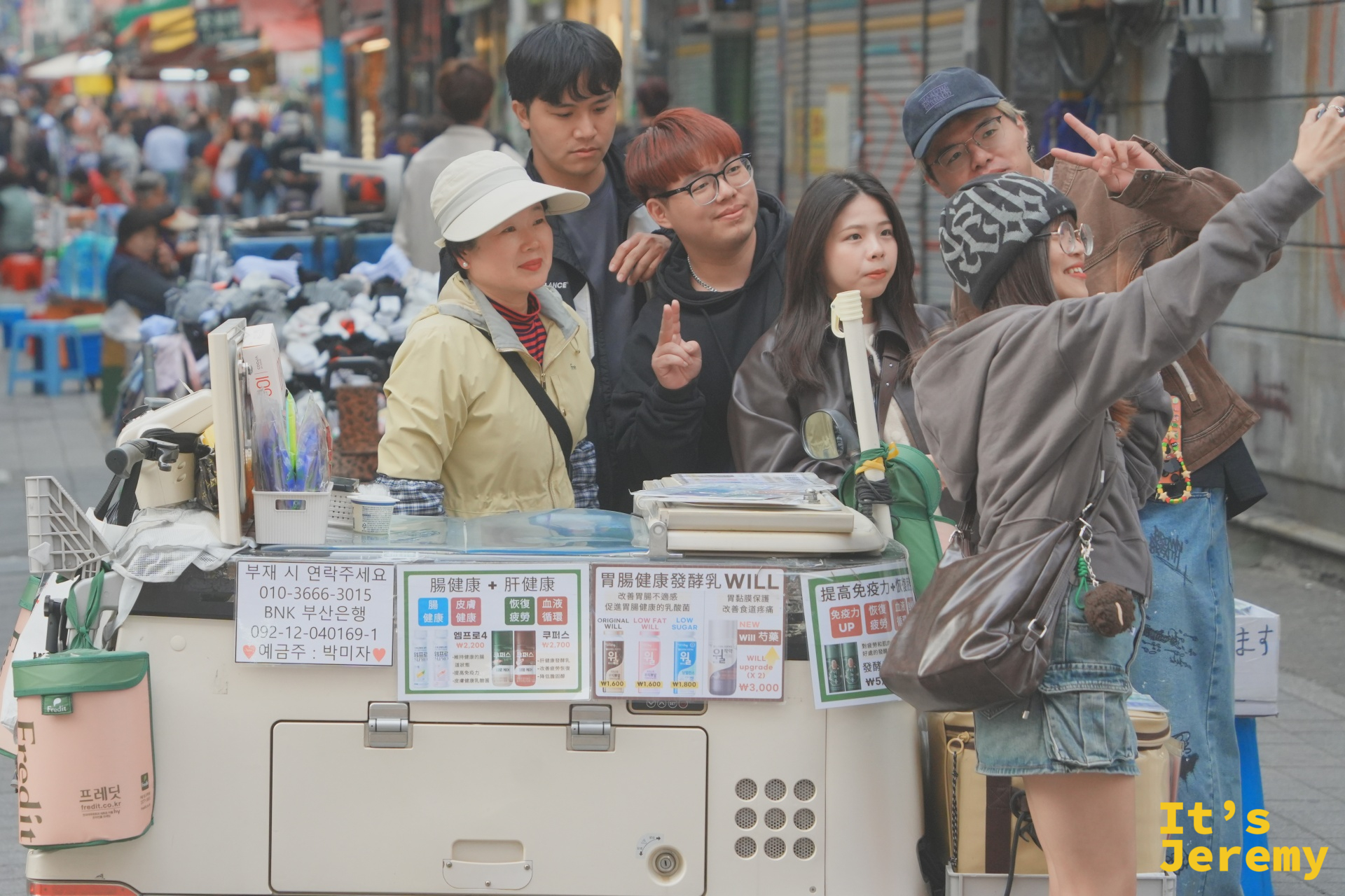 在國際市場的街頭攤車前，大家湊在一起笑著自拍，車上的中日文廣告牌是最釜山的背景